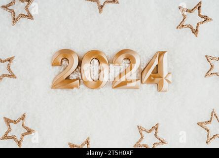 Grußkarte - Happy New Year mit Zahlen 2024 und goldenen Sternen auf künstlichem schneeweißen Hintergrund. Minimales Urlaubskonzept. Draufsicht. Flache Lagen Stockfoto