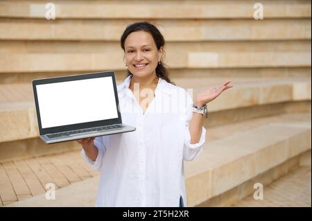 Selbstbewusste Verkäuferin, Händlerin, freischaffende Unternehmerin, die in die Kamera blickt und einen Laptop mit weißem Digitalbildschirm hält. Cop Stockfoto