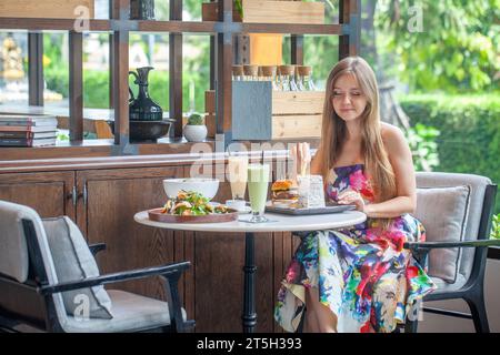 Entspanntes weibliches Diner in gemustertem Sommerkleid bietet ein Menü Stockfoto