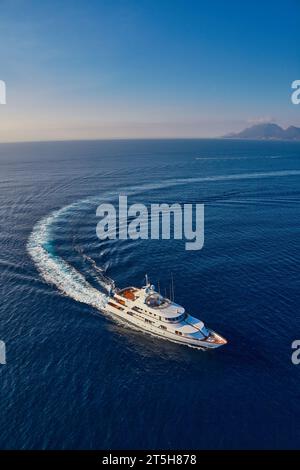 Luftbild einer weißen Superyacht, die im glitzernden blauen Mittelmeer zum Hafen fährt. Stockfoto