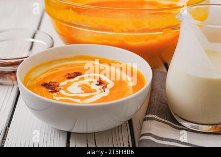 Gebratene Butternusskürbis-Suppe, serviert mit knusprigem Speck und schwerer Creme, Nahaufnahme in einer Schüssel auf einem weißen Holzbrett Stockfoto