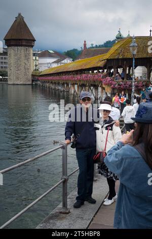 Luzern, Schweiz, - 26. August 2023: Lächelnde asiatische Touristen machen Fotos und Selfies bei schlechtem Wetter vor der Kapellbrücke Stockfoto