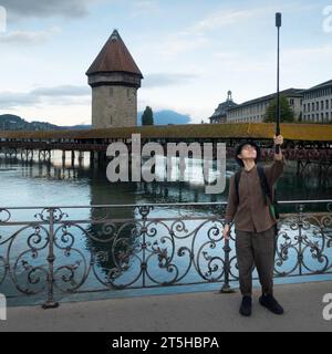 Luzern, Schweiz - 26. August 2023: Konzentrierter asiatischer Tourist macht Selfie bei schlechtem Wetter vor der Kapellbrücke Stockfoto