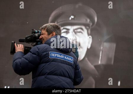 Moskau, Russland. November 2023. Ein Kameramann des Channel One Russia dreht eine Geschichte vor dem Hintergrund eines Porträts von Josef Stalin über ein Freilichtmuseum auf dem Roten Platz in Moskau; das Museum wurde anlässlich des 82. Jahrestages der historischen Parade des Roten Platzes am 7. November 1941 eröffnet, als Truppen der Roten Armee an die Front des Zweiten Weltkriegs zogen, um Moskau vor den Nazi-Truppen zu verteidigen. das Patch lautet „The Channel One“ Stockfoto