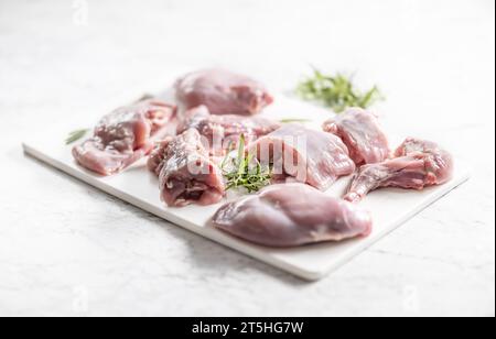 Stücke von portioniertem Kaninchen mit Rosmarin auf einem weißen Schneidebrett. Stockfoto