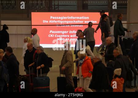 Hamburg, Deutschland. November 2023. Reisende sind im Terminal 1 am Flughafen Hamburg unterwegs, ein Neonschild mit der Aufschrift „die Check-in-Schalter werden in Kürze besetzt sein“. Tausende von Fluggästen waren von der Geiselnahme am Hamburger Flughafen am Samstagabend betroffen und Hunderte von Flügen wurden storniert. Quelle: Bodo Marks/dpa/Alamy Live News Stockfoto