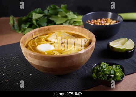 Typisches peruanisches Gericht, bekannt als Hühnersuppe, in einer Holzschale mit Zitrone und Schnittlauch. Stockfoto