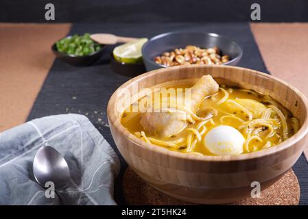 Typisches peruanisches Gericht, bekannt als Hühnersuppe, in einer Holzschale mit Zitrone und Schnittlauch. Stockfoto