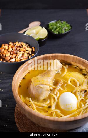 Typisches peruanisches Gericht, bekannt als Hühnersuppe, in einer Holzschale mit Zitrone und Schnittlauch. Stockfoto