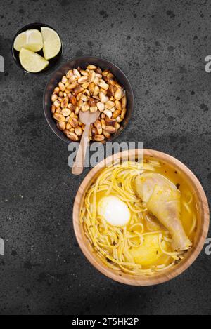 Typisches peruanisches Gericht, bekannt als Hühnersuppe, in einer Holzschale mit Zitrone und Schnittlauch. Stockfoto