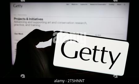 Person mit Handy und Logo der US-Kunststiftung J. Paul Getty Trust vor der Webseite. Schwerpunkt auf dem Display des Telefons. Stockfoto
