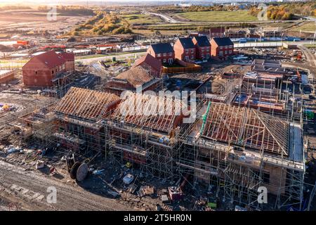 Luftaufnahme einer Baustelle mit neugebauten, energieeffizienten Häusern, die mit freiliegenden Dachsparren gebaut werden und von einem Gerüst mit Co umgeben sind Stockfoto
