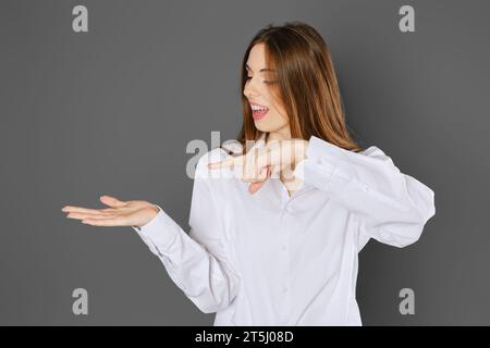 Eine junge Frau, die ein weißes Hemd trägt, das mit dem Zeigefinger auf ihre Handfläche zeigt Stockfoto
