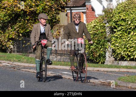 November 2023. Teilnehmer am London to Brighton Veteran Car Run 2023 durch West Sussex, England, Großbritannien. Die Route des beliebten jährlichen Events dauert 60 km. Im Bild: Zwei Männer, die alte Fahrräder in Retro-Tweed-Kleidung fahren, einer mit einem Fahrradhelm aus Leder. Links (Nummer 708) ein 1895 Crypto Cycle Standardmodell und rechts (Nr. 705) ein 1891 New Mail Sicherheitsfahrrad. Stockfoto