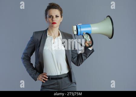 Stilvolle 40 Jahre alte Geschäftsfrau in grauem Anzug mit Megaphon isoliert auf Grau. Stockfoto