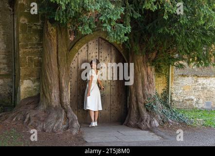 Stau on the Wold, Cotswolds, Worcestershire, Großbritannien - 14. September 2022 - schöne Frau in einem weißen Kleid und stehend an einer Tür nach hinten Stockfoto