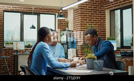Wütender Mann, der Akten in den Vorstandssitz wirft und sich gestresst fühlt, nachdem das Team keinen neuen Entwicklungsplan erhalten hat. Manager in Afrika-amerika ist wütend und frustriert über die Ergebnisse der Büroarbeit. Stockfoto