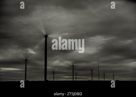 Traumhafte Vision von Windturbinen aus erneuerbaren Energien an einem grauen Tag mit turbulenten Wolken und wechselnden Mustern von Helligkeit und Dunkelheit. Stockfoto