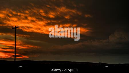 Einsamer Versorgungsmast und die letzten Momente des stürmischen Sonnenuntergangs im üppigen Sommer, der zu schwarz wird. Stockfoto