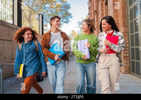 Eine Gruppe lächelnder Teenager-Schüler, die vor dem Unterricht laufen, lachen und miteinander reden. Verschiedene Klassenkameraden mit Notizbüchern und Rucksäcken unterwegs an der Universität. Mitarbeiter der Akademie. Hochwertige Fotos Stockfoto