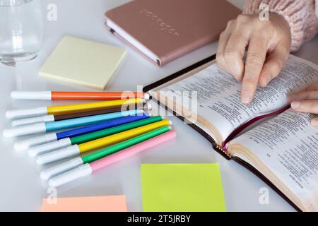 Hand hält heiliges Bibelbuch offen und zeigt auf inspirierende Verse. Christliches biblisches Studium, Lesen, Schreiben, Notizen mit bunten Markierungen machen. Stockfoto