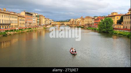 Florenz, Italien. 2013. Touristen in einem Boot auf dem Fluss Arno in der Nähe der Brücke Ponte Vecchio mit alten Gebäuden am Ufer des Flusses. Nur redaktionelle Verwendung. Stockfoto