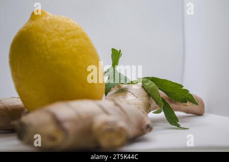 Ein weißer Tisch mit zwei gelben Zitronen, einem Stück frischen Ingwer und einem grünen Blatt Stockfoto