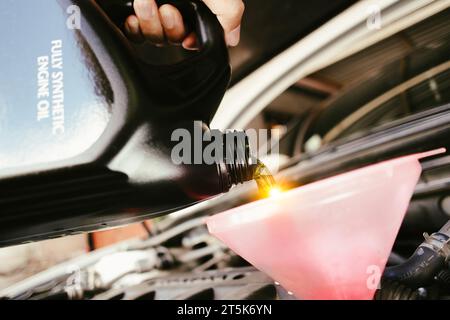 Ein Automechaniker gießt neues Motoröl in einen Trichter in das Wartungskonzept für Automotoren Stockfoto