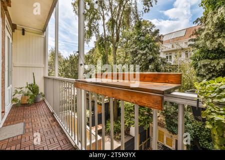 Ein Balkon mit Ziegelboden und weißen Geländern, umgeben von üppigen grünen Bäumen auf der anderen Seite des Hauses Stockfoto