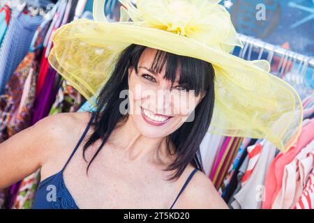 Lächelnde Brünette Frau, die einen Big Sun Hut auf dem Markt modelliert. Stockfoto