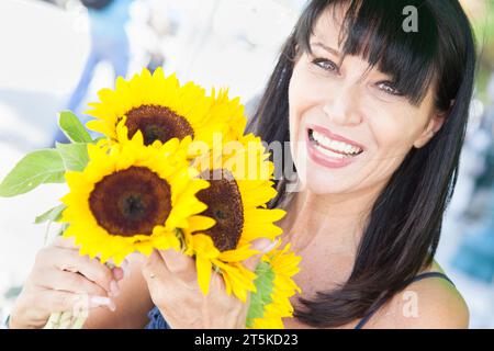 Happy Brünette Woman hält einen frischen Sonnenblumenstrauß auf dem Bauernmarkt. Stockfoto