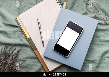 Ansicht von oben auf Büromaterial, Smartphone mit leerem Mockup-Bildschirm, über Notebooks, Stifte, Brillen Stockfoto