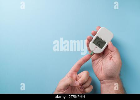 Der Mann misst den Blutzuckerspiegel mit einem Glukometer. Diabetes-Konzept auf blauem Hintergrund Stockfoto