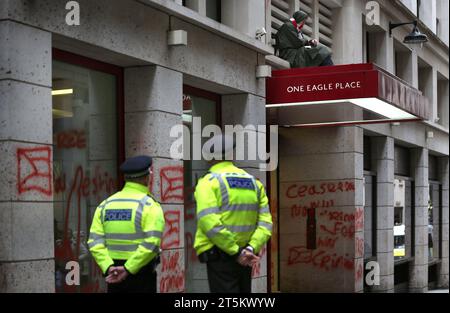 Polizisten beobachten einen Aktivisten, der auf dem Vordach von Leonardos Büros sitzt. Aktivisten der Palästinensischen Aktion besetzen und zielen den italienischen Rüstungsgiganten Leonardo in ihrem Londoner Hauptquartier und schließen sie ab. Leonardo beliefert Israel mit Kampfjets und Waffen, die derzeit im Gazastreifen eingesetzt werden. Die Palästinensische Aktion verlangt, dass Waffenunternehmen, die Waffen für Israel bereitstellen, dauerhaft stillgelegt werden. Sie haben angekündigt, dass Unternehmen, die Waffen an die israelischen Streitkräfte verkaufen, und ihre Partnerunternehmen mit direkten Maßnahmen ins Visier genommen werden. Diese Aktionen sollen hervorgehoben werden Stockfoto