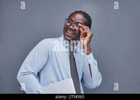 Junger afroamerikanischer Mann auf grauem Hintergrund, der seine Brille anpasst Stockfoto