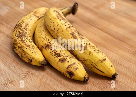 Drei reife Bananen auf einem hölzernen Schneidebrett. Stockfoto