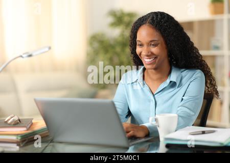 Glücklicher schwarzer Tele-Mitarbeiter, der zu Hause online mit einem Laptop arbeitet Stockfoto