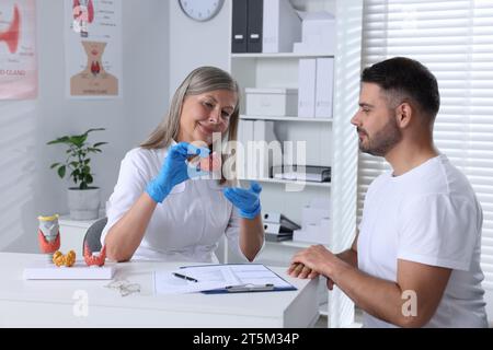 Endokrinologe zeigt Schilddrüsenmodell dem Patienten am Tisch im Krankenhaus Stockfoto
