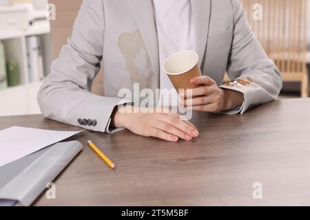 Frau zeigt Flecken von Kaffee auf ihrer Jacke an Holztisch drinnen, Nahaufnahme Stockfoto