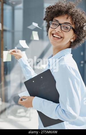 Ein Mädchen in einem modernen Büro hinter Glas verwendet Haftnotizen und macht Notizen Stockfoto