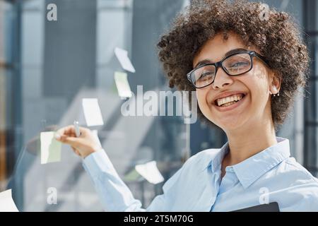 Ein Mädchen in einem modernen Büro hinter Glas verwendet Haftnotizen und macht Notizen Stockfoto