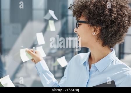 Ein Mädchen in einem modernen Büro hinter Glas verwendet Haftnotizen und macht Notizen Stockfoto