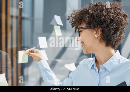 Ein Mädchen in einem modernen Büro hinter Glas verwendet Haftnotizen und macht Notizen Stockfoto