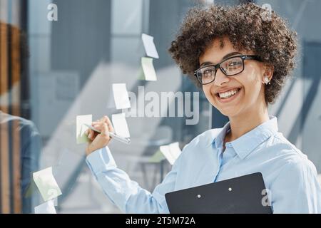 Ein Mädchen in einem modernen Büro hinter Glas verwendet Haftnotizen und macht Notizen Stockfoto