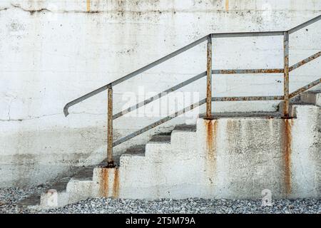 Rostige Metalltreppe gegen eine verwitterte, rissige Betonwand mit alten und rostbefleckten Stufen und Geländern Stockfoto