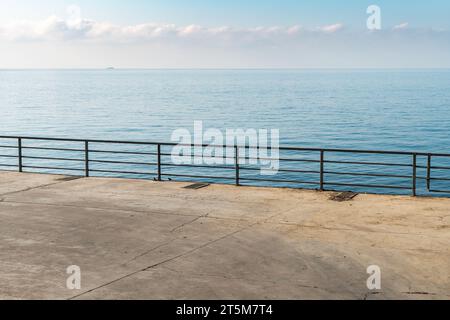 Leerer Betonboden mit Metallgeländern über ruhigem Meer an sonnigen Tagen. Stadtdamm und ruhige azurblaue Bucht im Resort. Reisen im Sommer Stockfoto