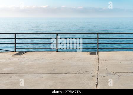 Leerer Betonboden mit Metallgeländern über ruhigem Meer an sonnigen Tagen. Stadtdamm und ruhige azurblaue Bucht im Resort. Reisen im Sommer Stockfoto