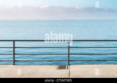 Leerer Betonboden mit Metallgeländern über ruhigem Meer an sonnigen Tagen. Stadtdamm und ruhige azurblaue Bucht im Resort. Reisen im Sommer Stockfoto