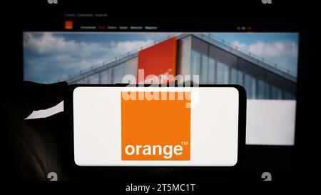 Person mit Smartphone und Logo des französischen Telekommunikationsunternehmens Orange S.A. vor der Website. Schwerpunkt auf dem Display des Telefons. Stockfoto