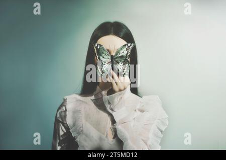 Frau hält einen Schmetterling vor ihrem Gesicht; abstraktes Konzept Stockfoto